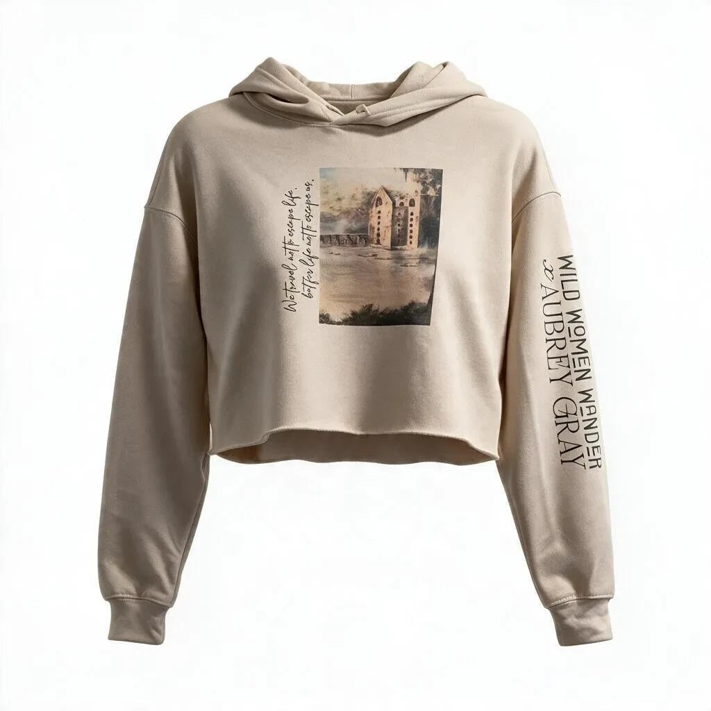 Beige cropped hoodie from the Wild Women Wander collection featuring a scenic landscape graphic and sleeve text.
